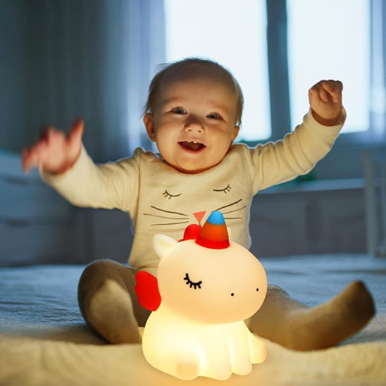 Bébé souriant jouant avec veilleuse bébé licorne